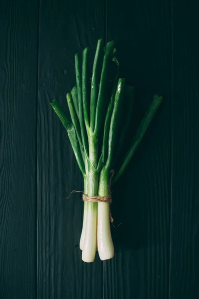 Oignons verts sur une planche de bois noir givré . — Photo