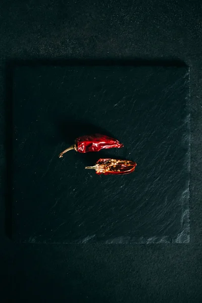 Chiles rojos secos calientes en un plato de pizarra sobre un fondo negro — Foto de Stock