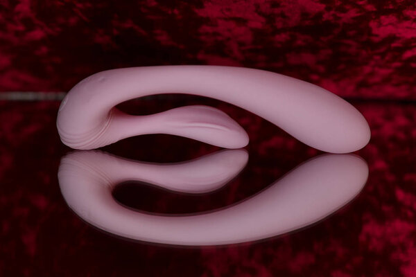 Pink futuristic vibrator with a process for clitoral stimulation. Photo sex toys on the mirror.