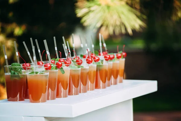 Dużo szklanek ze słomką z naturalnym sokiem na stole. Impreza na świeżym powietrzu. Domowej roboty kompot ozdobiony wiśniami i miętą — Zdjęcie stockowe