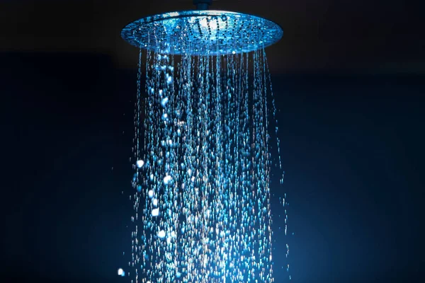 Water falling from the shower on a dark background with blue backlight in the aqua zone — 스톡 사진
