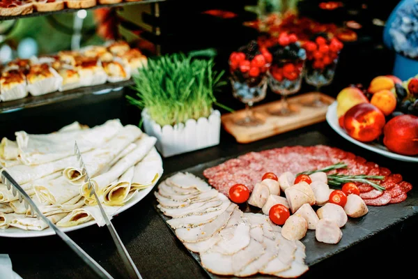 Ein Tisch mit verschiedenen Snacks und Scheiben. Essen bei einer Open-Air-Party. Mini-Burger und Canapes. Tisch mit Blumen und Gras dekoriert. — Stockfoto