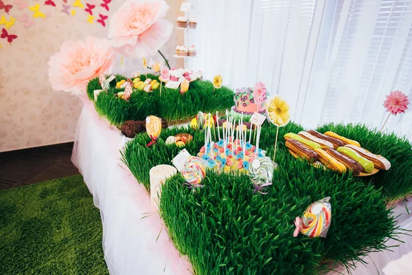 Stół z świątecznym tortem z mastyksowymi kwiatami i ciasteczkami. Kandy bar jest ozdobiony trawą, na której ciasto i lizaki — Zdjęcie stockowe
