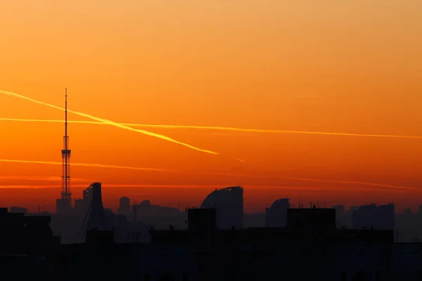 A television tower but against a background of bright orange sunset and the city. Traces of the plane in the sunset sky. — Stock Photo, Image