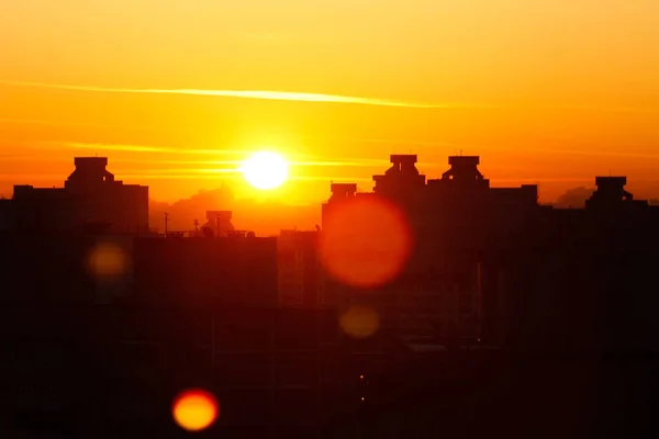 Oranje zonsondergang op de achtergrond van de stad. Silhouet van een bouwkraan. Foto met een schittering van de zon. Panorama van de stad. — Stockfoto
