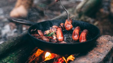 Kızarmış mantar ve sosisli pastırma. Ormanda ateşte, tavada. Doğada yiyecek. Yolda yemek pişirmek. Piknik