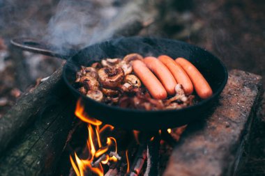 Kızarmış mantar ve sosisli pastırma. Ormanda ateşte, tavada. Doğada yiyecek. Yolda yemek pişirmek. Piknik
