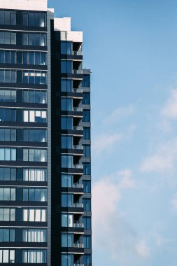 Geniş pencereli ve mavi gökyüzüne karşı siyah cepheli modern mesken binası. Bir yazıt için yer.