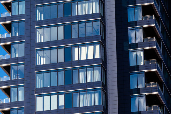 A modern residential building in dark blue with large glass windows against the sky. Skyscraper close up. Business building