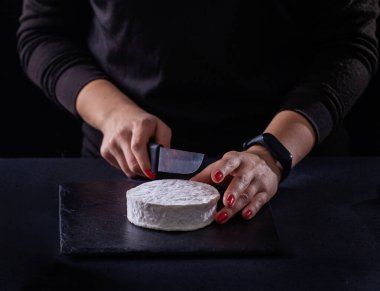 Koyu arkaplanda keçi peyniri dilimleyen bir kız..