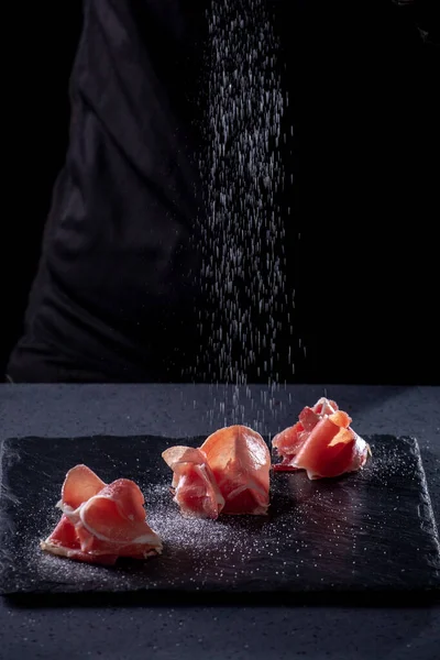 The chef is salting the bacon. Bacon on a stone plate on a dark background. — Stock Image Chef Salting Bacon Bacon Stone Plate Dark Background Stock Picture