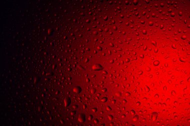 Kırmızı ışıkta cam üzerine su damlaları. Camın üzerine renkli ışıkların arka planına yağmur yağar. Arkaplan için soyut fotoğraf