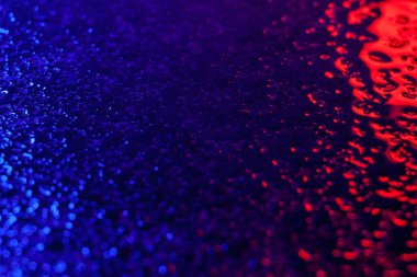 Islak yüzeydeki ışığın soyut yansıması. Islak yüzeyde mavi ve kırmızı neon ışık. Kaldırım üzerindeki ışığın yansıması. Suyun üzerinde parla