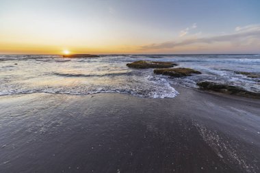 Pasifik Okyanusu 'nun ortasındaki su ufkunun altında batan güneş, Şili' nin vahşi sahillerinde alacakaranlıkla muhteşem ve renkli bir manzara oluşturuyor. Turuncu tonlu güzel gölgeler ve yansımalar.