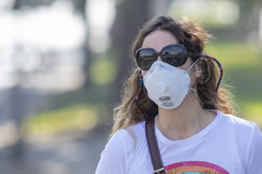 Gerçek insanlar portrelerle karşılaşır. Güneş gözlüklü bir kadın Coronavirus hastalığı enfeksiyonunu önlemek için Providencia sokaklarında maske koruması altında yürürken endişeleniyor.