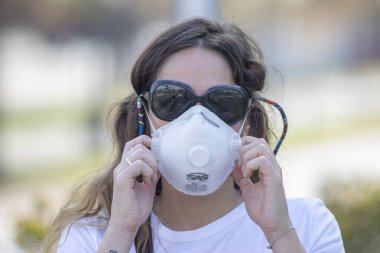 Gerçek insanlar portrelerle karşılaşır. Güneş gözlüklü bir kadın Coronavirus hastalığı enfeksiyonunu önlemek için Providencia sokaklarında maske koruması altında yürürken endişeleniyor.