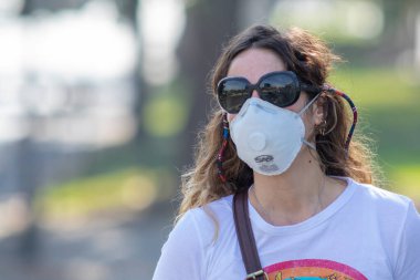 Gerçek insanlar portrelerle karşılaşır. Güneş gözlüklü bir kadın Coronavirus hastalığı enfeksiyonunu önlemek için Providencia sokaklarında maske koruması altında yürürken endişeleniyor.