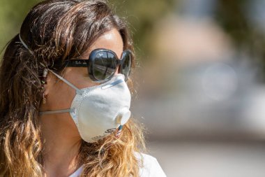 Gerçek insanlar portrelerle karşılaşır. Güneş gözlüklü bir kadın Coronavirus hastalığı enfeksiyonunu önlemek için Providencia sokaklarında maske koruması altında yürürken endişeleniyor.