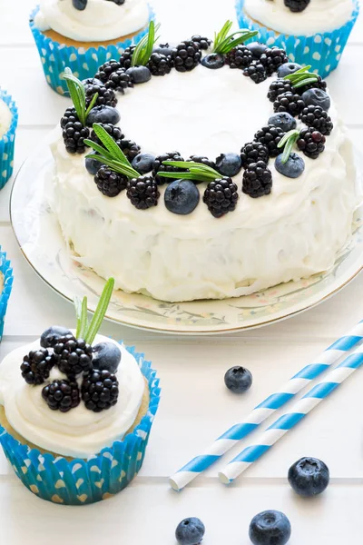 Cupcakes caseiros e bolo com cobertura, mirtilos, amoras e folhas de alecrim — Fotografia de Stock