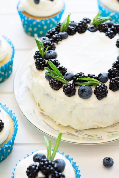 Cupcakes caseiros e bolo com cobertura, mirtilos, amoras e folhas de alecrim — Fotografia de Stock