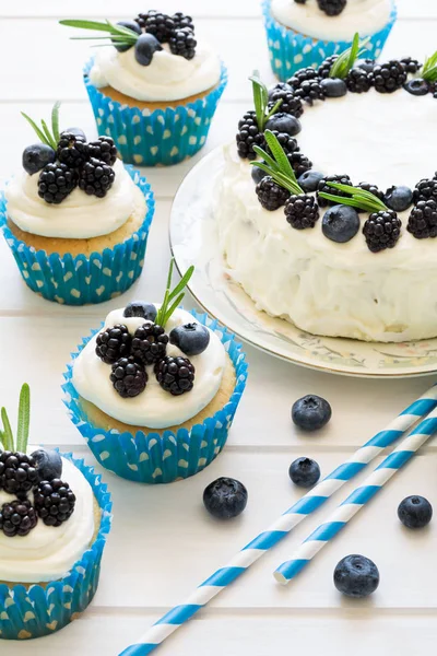 Домашние кексы и торт с глазурью, черникой, ежевикой и листьями розмарина — стоковое фото