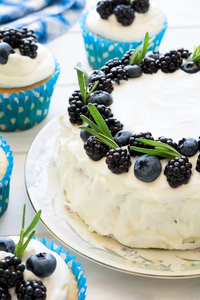 Домашние кексы и торт с глазурью, черникой, ежевикой и листьями розмарина — стоковое фото