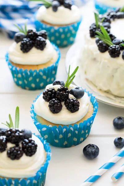 Cupcakes caseiros e bolo com cobertura, mirtilos, amoras e folhas de alecrim — Fotografia de Stock