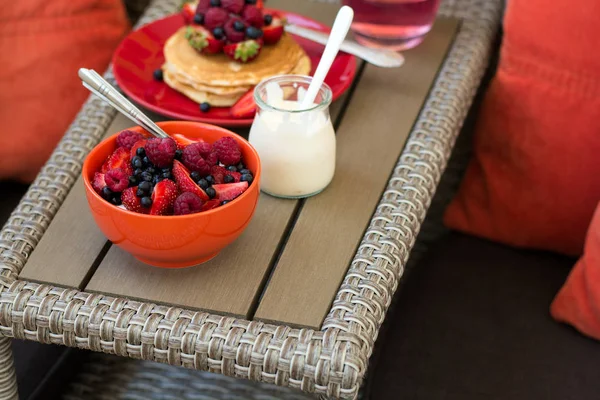 Hälsosam frukost på trädgårdsmöbler: keso med gräddfil, jordgubbar, hallon och blåbär, pannkakor, yoghurt och juice — Stockfoto