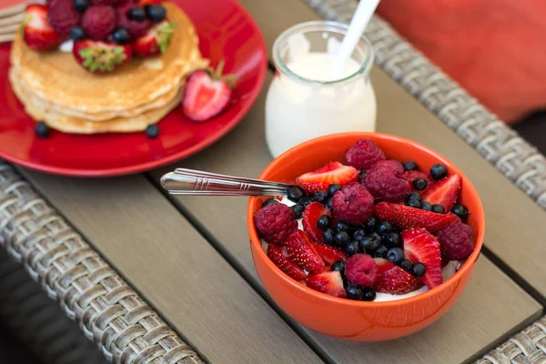 Здоровый завтрак на садовой мебели: творог со сметаной, клубника, малина и черника, блины, йогурт и сок — стоковое фото