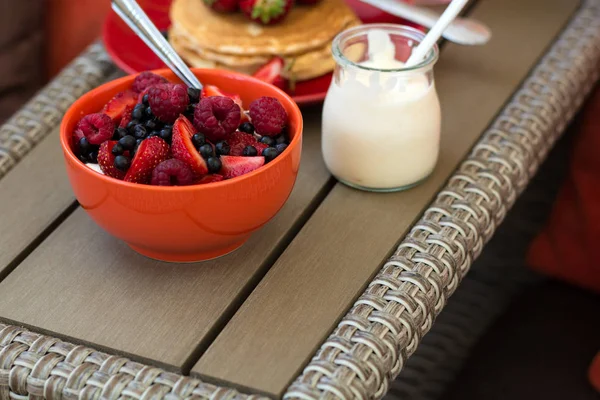 Hälsosam frukost på trädgårdsmöbler: keso med gräddfil, jordgubbar, hallon och blåbär, pannkakor, yoghurt och juice — Stockfoto