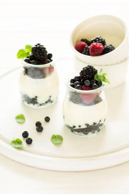 Sağlıklı Kahvaltı: yoğurt çilek, yaban mersini ve blackberry ile dekore edilmiş nane yaprakları Beyaz ahşap tablo