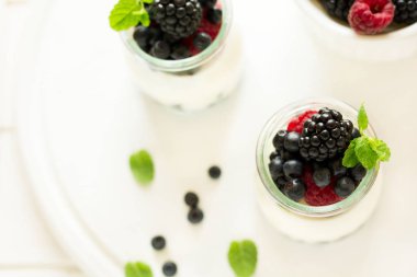 Sağlıklı Kahvaltı: yoğurt çilek, yaban mersini ve blackberry ile dekore edilmiş nane yaprakları Beyaz ahşap tablo