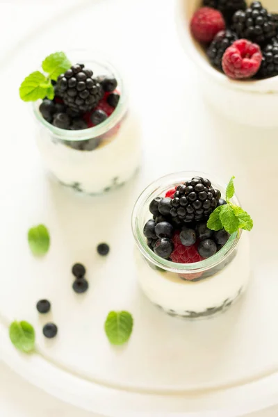 Здоровый завтрак: йогурт с клубникой, черникой и ежевикой украшенные листья мяты на белом деревянном столе — стоковое фото