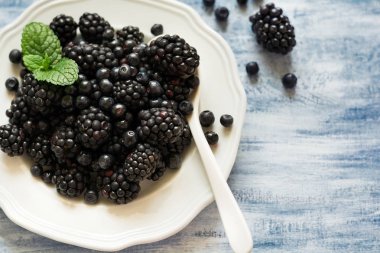 Böğürtlen ve mavi ahşap arka plan üzerinde yaban mersini ile plaka. Üstten Görünüm