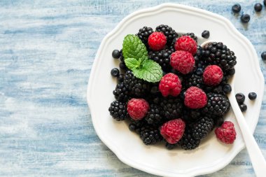 Böğürtlen ve mavi ahşap arka plan üzerinde yaban mersini ile plaka. Üstten Görünüm