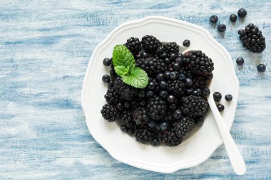 Böğürtlen ve mavi ahşap arka plan üzerinde yaban mersini ile plaka. Üstten Görünüm