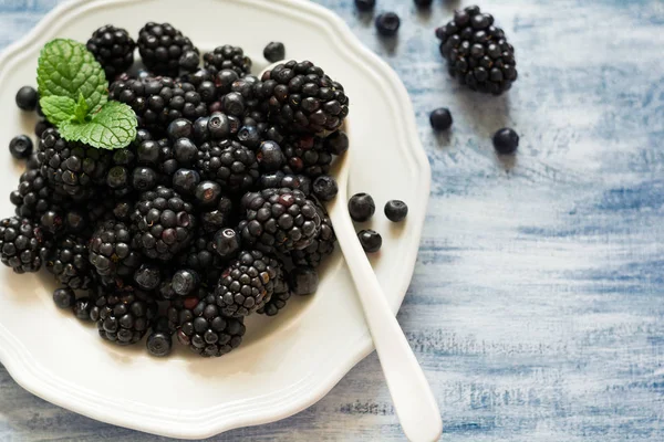 Böğürtlen ve mavi ahşap arka plan üzerinde yaban mersini ile plaka. Üstten Görünüm