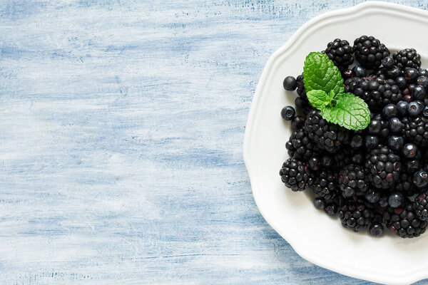 Plate with blackberries and blueberries on blue wooden background. Top view