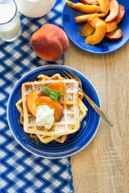 Sağlıklı Kahvaltı: Belçika waffle şeftali dilimleri ve krema ile dekore edilmiş olan nane yaprakları ve mavi peçete 
