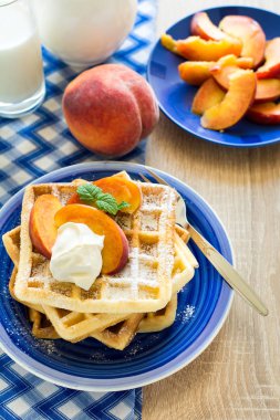 Sağlıklı Kahvaltı: Belçika waffle şeftali dilimleri ve krema ile dekore edilmiş olan nane yaprakları ve mavi peçete 