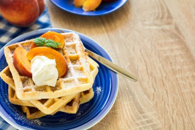 Sağlıklı Kahvaltı: Belçika waffle şeftali dilimleri ve krema ile dekore edilmiş olan nane yaprakları ve mavi peçete 