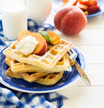 Sağlıklı Kahvaltı: Belçika waffle şeftali dilimleri ve krema ile dekore edilmiş olan nane yaprakları ve mavi peçete 