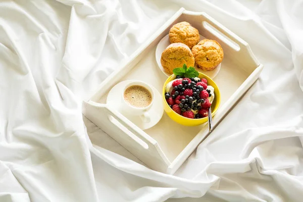 Wooden tray with tasty breakfast on bed. Espresso, banana muffins, cottage cheese with blueberry and raspberry