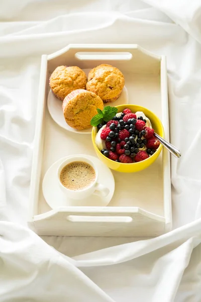 Wooden tray with tasty breakfast on bed. Эспрессо, банановые кексы, творог с черникой и малиной — стоковое фото
