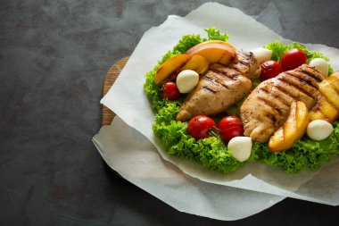 Barbekü: ızgara tavuk göğsü, domates, şeftali dilimleri ve ahşap masa üzerinde mini Mozzarella peyniri