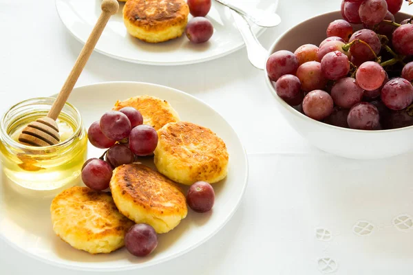 Сніданок з міні-сирниками, виноградом, вершками та медом на білій тарілці — стокове фото
