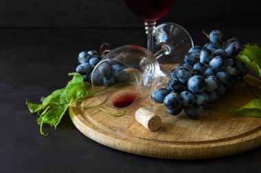 İki kadehlerin kırmızı şarap ve üzüm asma yaprağı koyu ahşap masa üzerine dekore edilmiştir.