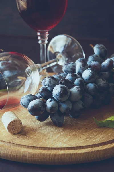İki kadehlerin kırmızı şarap ve üzüm asma yaprağı koyu ahşap masa üzerine dekore edilmiştir.