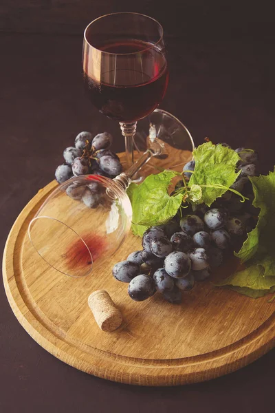 İki kadehlerin kırmızı şarap ve üzüm asma yaprağı koyu ahşap masa üzerine dekore edilmiştir. — Stok fotoğraf