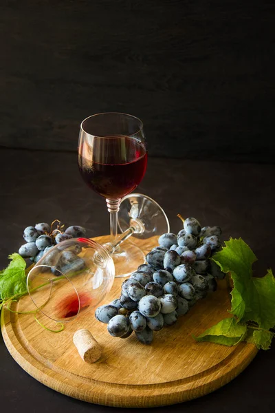 Dwa kieliszki z czerwonego wina i winogron urządzone liści winorośli na ciemne drewniane biurko — Zdjęcie stockowe